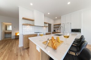A modern kitchen with white cabinetry, a wooden countertop, and a dining area with black chairs.