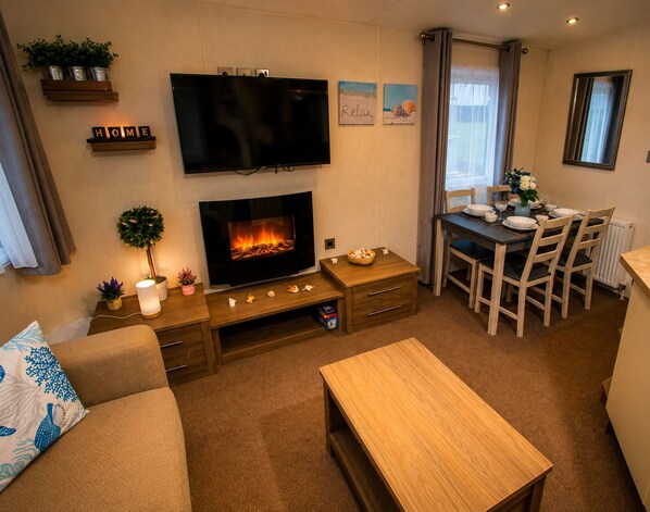 A living room with a fireplace, a television, a dining area with chairs and a table, and a sofa with decorative pillows.