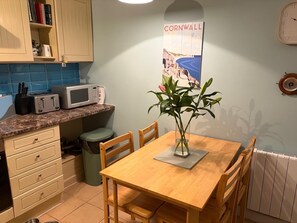 Een keuken met een houten tafel, stoelen, een magnetron en een poster aan de muur.