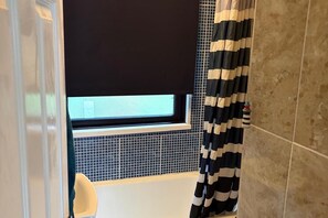 Een badkamer met een bad, een raam en een zwart-wit gestreept douchegordijn.