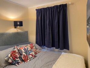 Een hotelkamer met een bed, een flatscreen televisie aan de muur en een groot raam met donkere gordijnen.