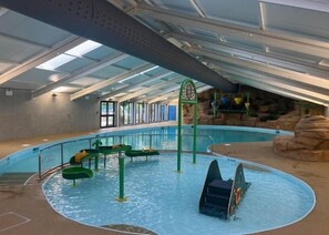 Een binnenzwembad met een centrale waterglijbaan, een duikplank en een rotsformatie als achtergrond.