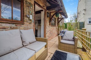 A traditional brick building with a wooden porch, a wicker sofa, and a chair. - Cottage - Sleeps 4 - Parking (Evesham)