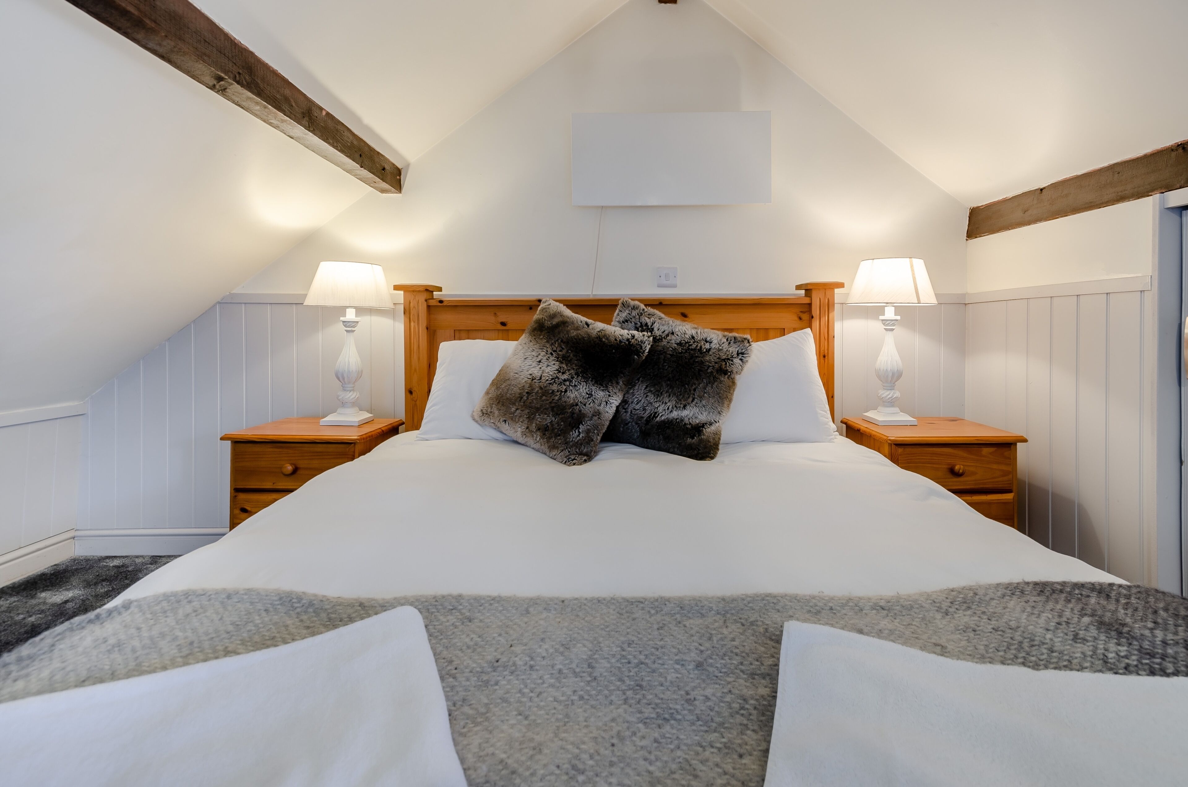 Quarto com cama grande, duas mesas de cabeceira e vigas de madeira no teto.