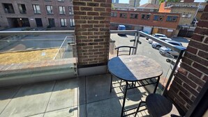 Varanda com mesa e cadeiras, com vista para um estacionamento e edifícios.