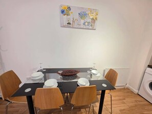 A dining area with a table set for four, surrounded by chairs, and a wall-mounted painting above. - Cozy City 1Br w/Balcony at the Heart of Stratford (London)