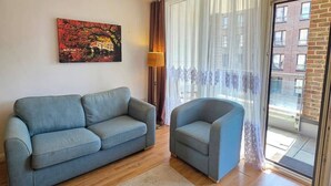 Sala de estar com sofá, poltrona, um quadro, luminária e vista através de uma porta de vidro.