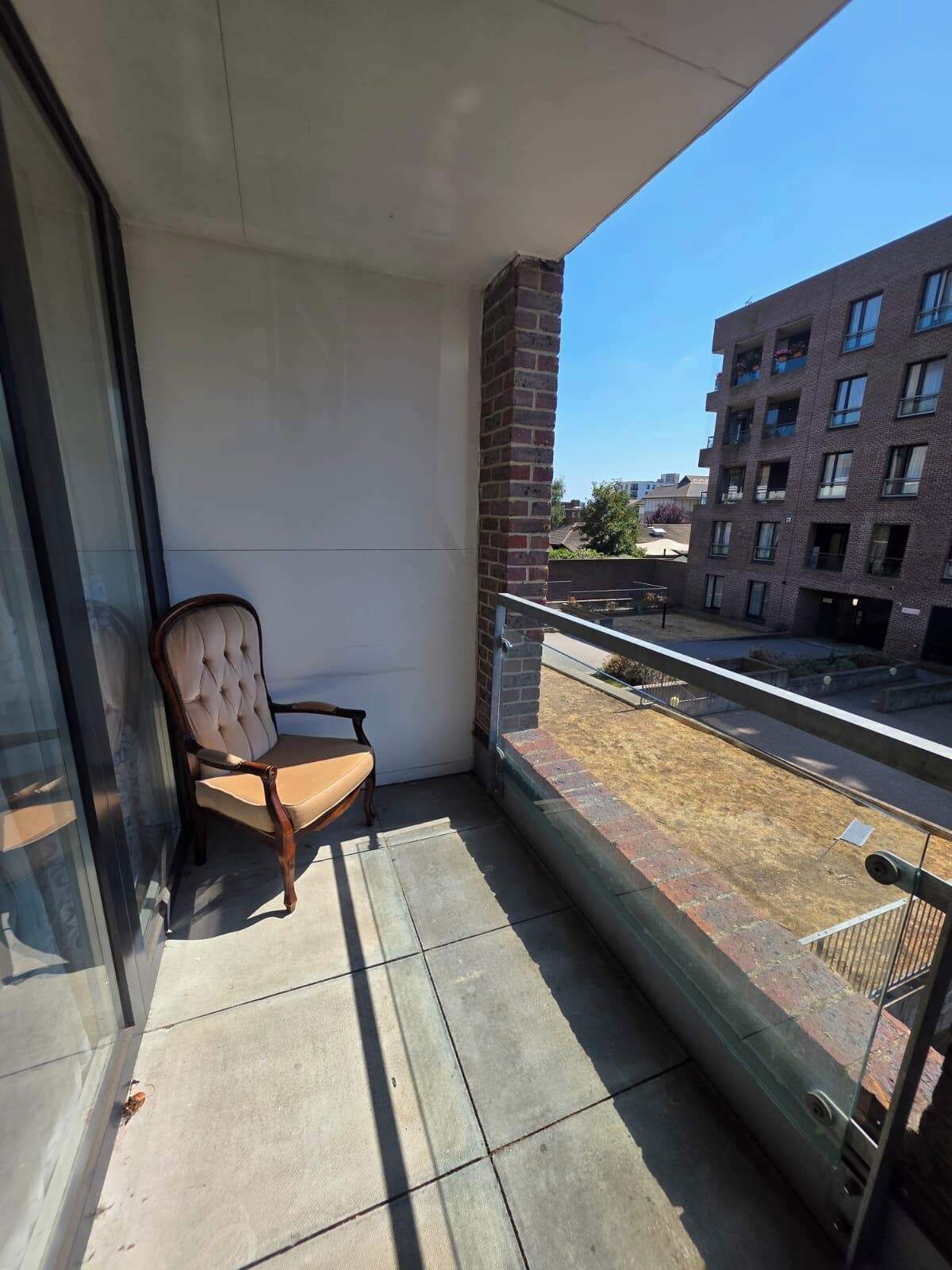 A balcony with a cushioned chair, a glass door, and a view of a brick building.