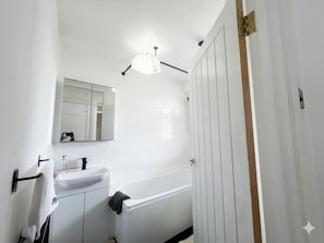 Une salle de bain avec un lavabo blanc, un miroir et une baignoire.