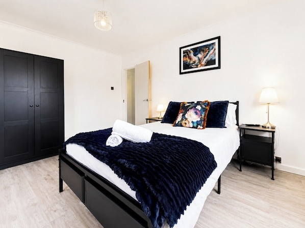 Une chambre à coucher moderne avec un lit, une table de chevet, une lampe, une armoire et un tableau au mur.