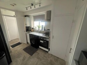 A compact kitchen with a washing machine, a stove, and a sink. - Central Wimbledon Apartment with 2 Bedrooms, Free Parking, Fast WIFI (London)