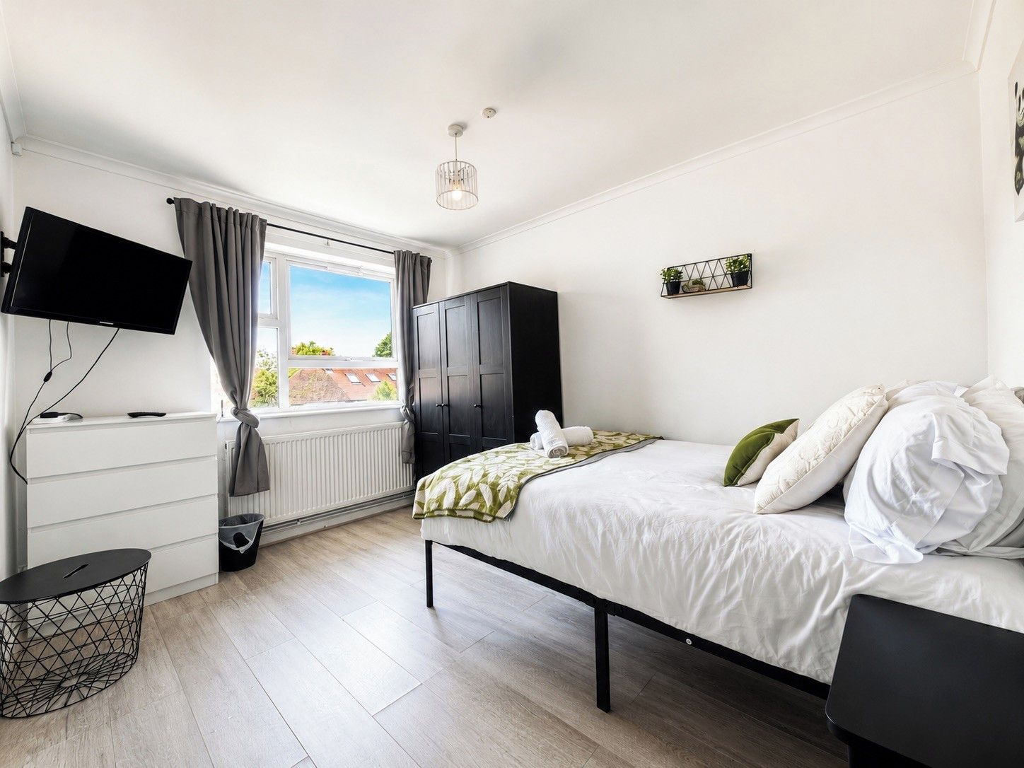 A bedroom with a bed, a TV, a wardrobe, and a window.