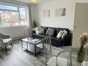 Un salon moderne avec un canapé, une table basse en verre, un fauteuil et une vue sur l’extérieur.