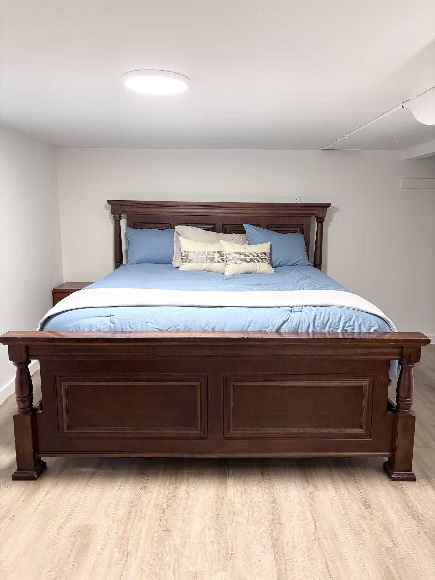 A bedroom with a wooden bed, a white ceiling, and a light fixture.