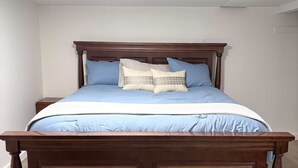 A bedroom with a wooden bed, a white ceiling, and a light fixture. - Spacious & Cozy Suite Getaway in KC Area · No Stairs (Blue Springs)
