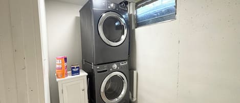 A compact laundry room with stacked washer and dryer units, a cabinet, and a window.
