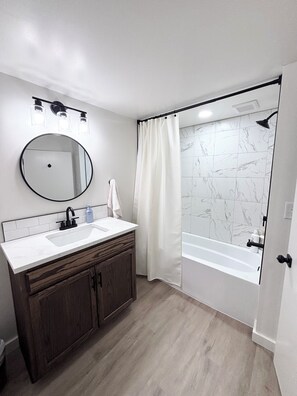 Une salle de bain avec un miroir rond, un lavabo, une douche avec un rideau et une baignoire.