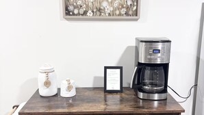 A wooden coffee station with a framed floral artwork above it. - Spacious & Cozy Suite Getaway in KC Area · No Stairs (Blue Springs)