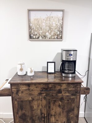 Un meuble en bois servant de coin café, avec une œuvre d’art florale encadrée placée au-dessus.