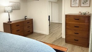A bedroom with a bed, dresser, and a nightstand. There is a door leading to another room. - Spacious & Cozy Suite Getaway in KC Area · No Stairs (Blue Springs)