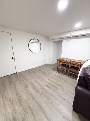 Une pièce avec une table et des chaises de salle à manger en bois, une porte blanche et un miroir rond accroché au mur.
