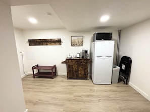Una cocina compacta con un refrigerador blanco, una cafetera y un banco de madera.