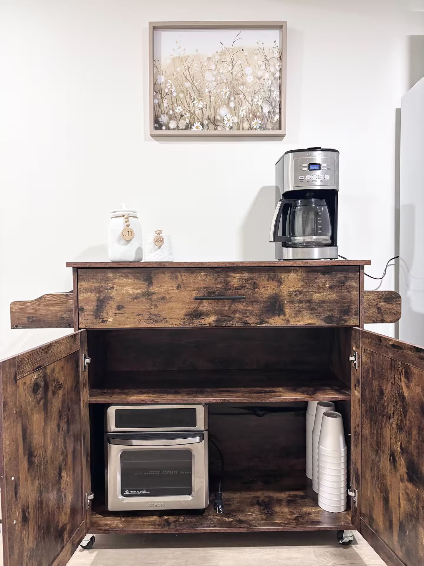 Una kitchenette con cafetera, tostadora y un cuadro con motivos florales en la pared.