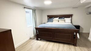 A bedroom with a large bed, a window with curtains, and a wooden floor. - Spacious & Cozy Suite Getaway in KC Area · No Stairs (Blue Springs)