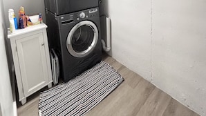 A laundry room with two stacked washing machines, a cabinet with cleaning supplies, and a window with blinds. - Spacious & Cozy Suite Getaway in KC Area · No Stairs (Blue Springs)