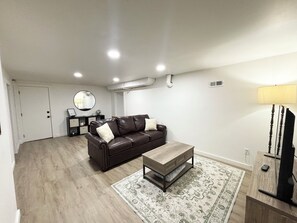 A living room with a brown leather sofa, a wooden coffee table, a patterned rug, a lamp, and a television. - Spacious & Cozy Suite Getaway in KC Area · No Stairs (Blue Springs)