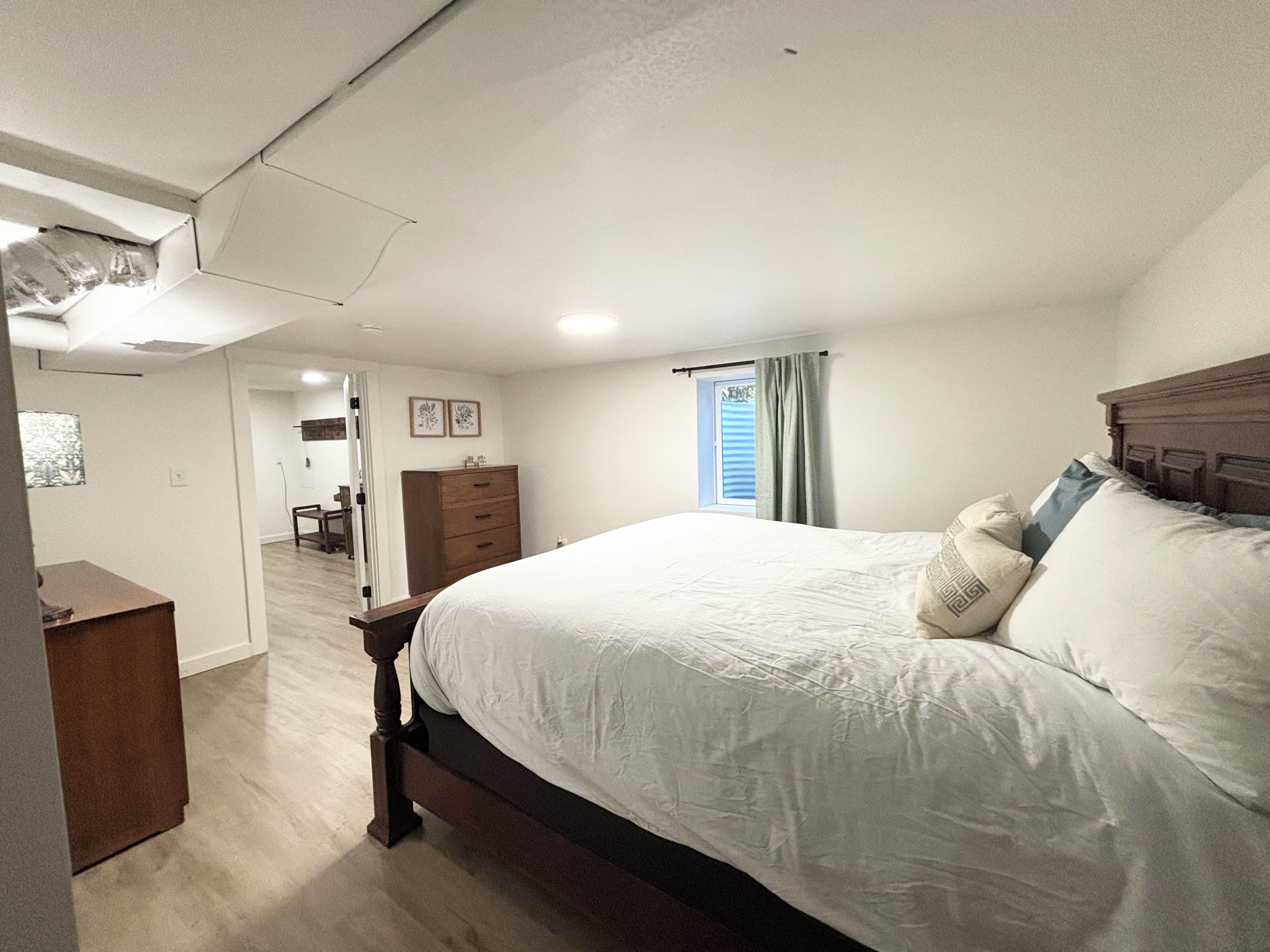 A bedroom with a large bed, a wooden dresser, and a window with curtains.