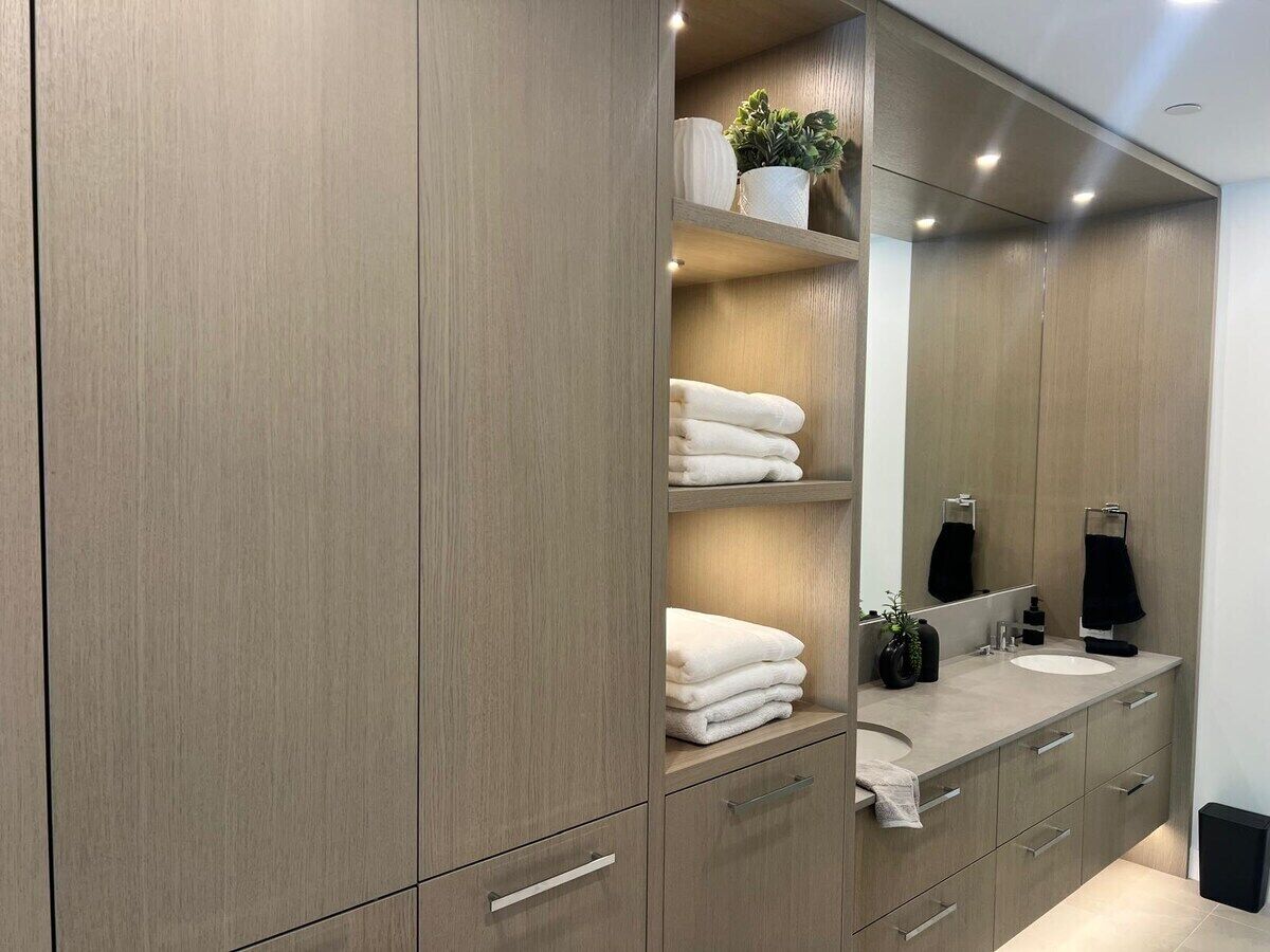 Une salle de bain moderne avec un grand miroir, des meubles en bois et un plan de toilette doté d’un lavabo et d’articles de toilette.