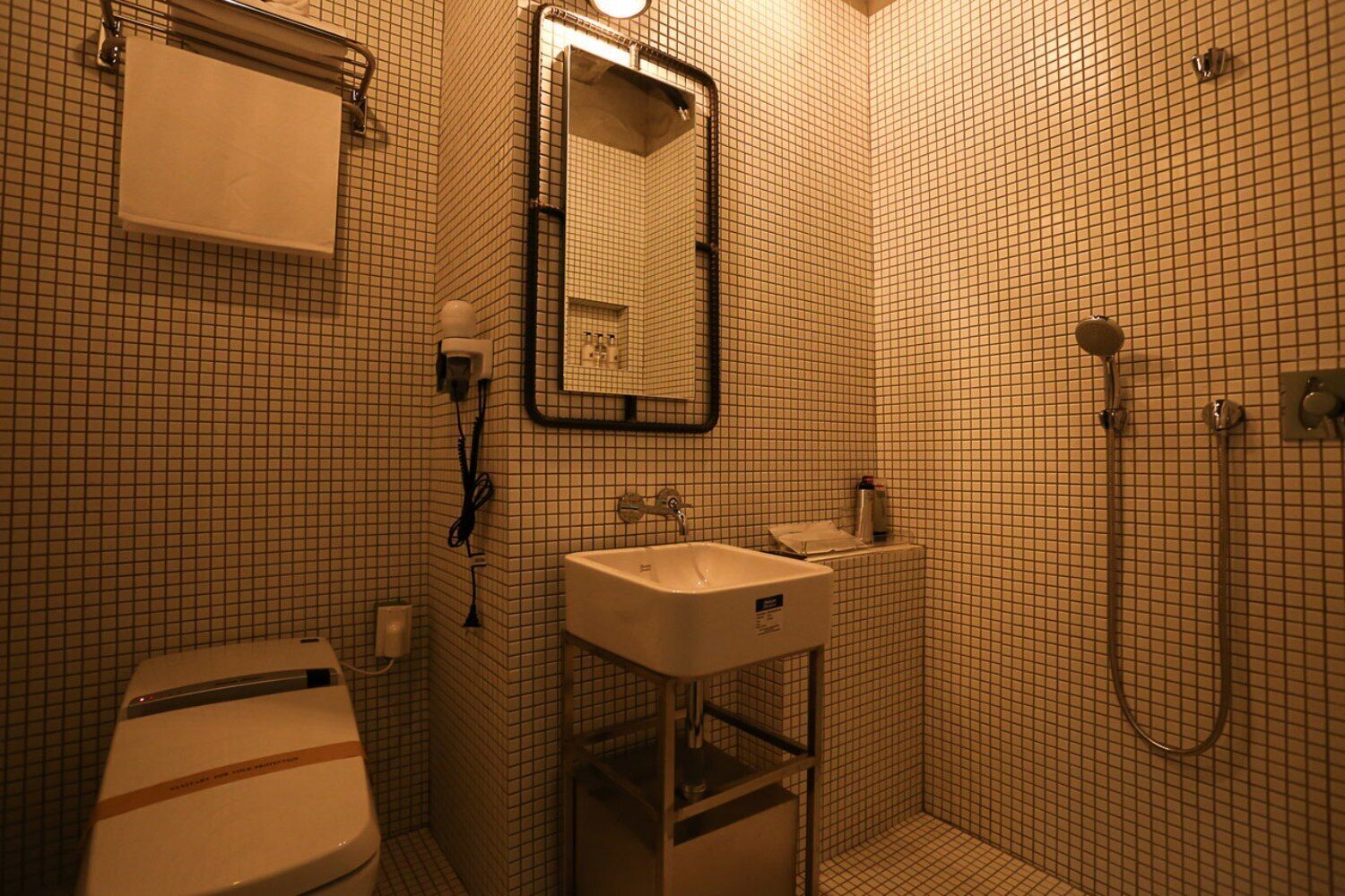 A small, tiled bathroom with a toilet, sink, and shower.