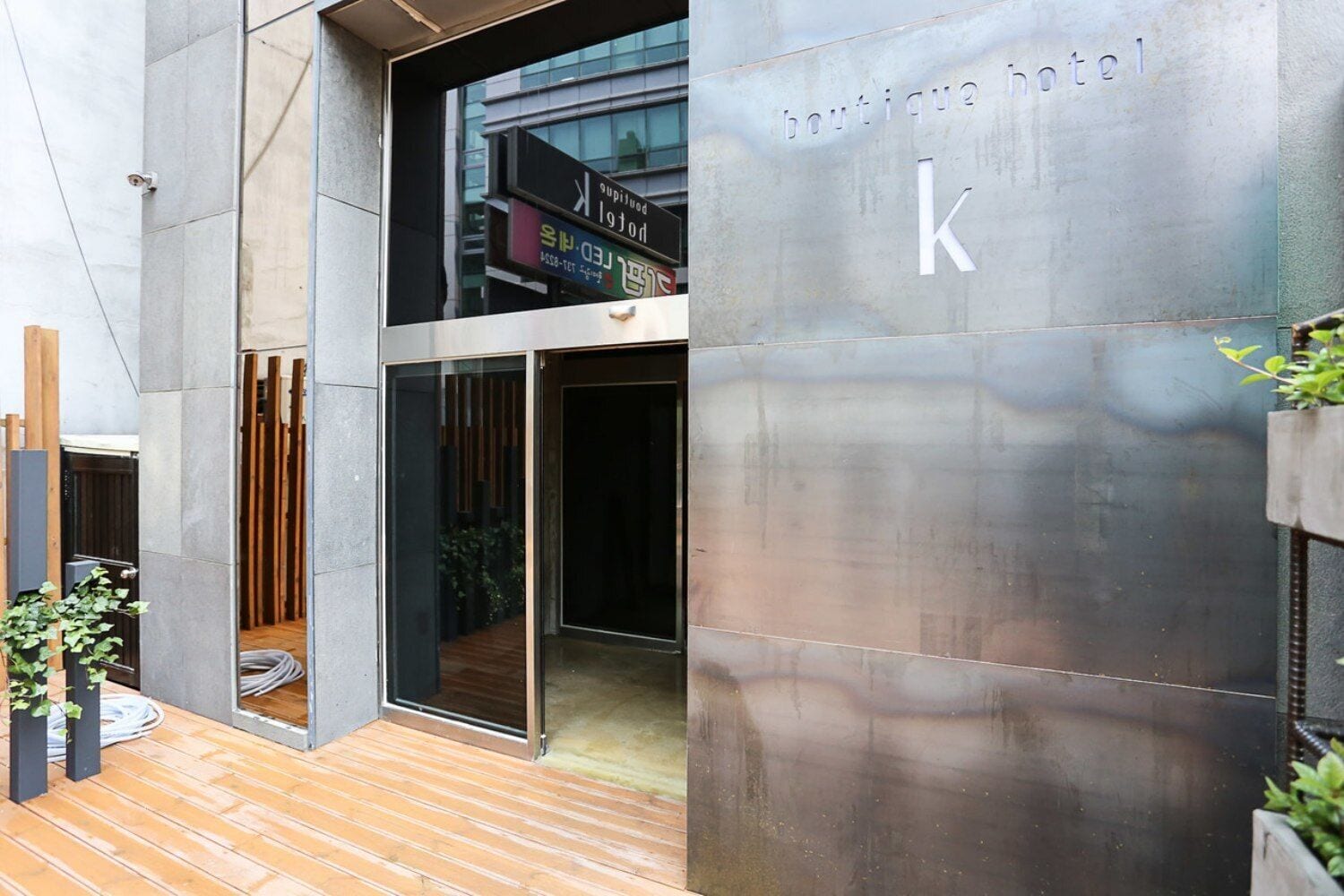 A modern building with a large glass entrance, a visible sign for 'boutique hotel k', and a wooden deck area.
