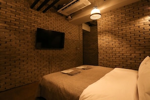 Een kamer met een bakstenen muur, een flatscreen-tv boven een bed en een hanglamp.