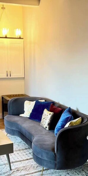 A modern living room with a curved grey sofa, a small wooden side table, and a white cabinet. - Every Room Water View|Modern Coastal Stay w Patio (Federal Way)