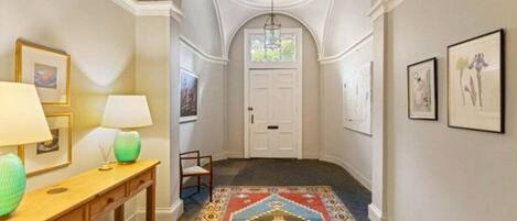 Un pasillo con alfombra estampada, una consola de madera con lámparas, obras enmarcadas en las paredes y una puerta blanca al final.