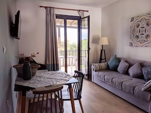A room with a dining table, chairs, a sofa, a lamp, and a view through a glass door. - Villa Karina Near Achladies Beach (Skiathos)