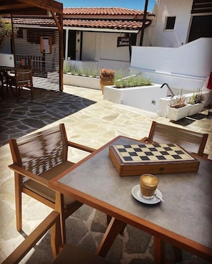 A wooden table with a chessboard and a cup of coffee, surrounded by wicker chairs, in an outdoor patio area with stone flooring and potted plants. - Villa Karina Near Achladies Beach (Skiathos)