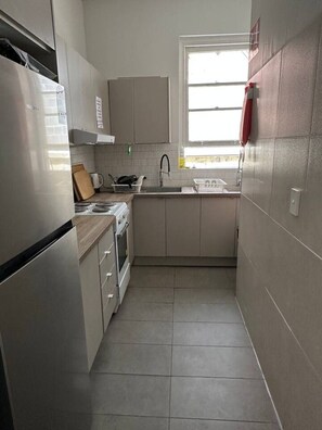 A compact kitchen with a refrigerator, stove, sink, and cabinets. - 5 minutes to Central Sydney - Lord Raglan Hotel (Alexandria)