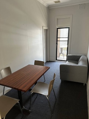 A room with a wooden table, four chairs, a grey sofa, and a window with a metal screen. - 5 mins to Central Sydney Lord Raglan Hotel (Alexandria)