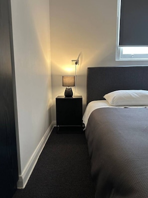 A hotel room with a bed, a nightstand with a lamp, a power outlet, and a window. - 5 mins to Central Sydney Lord Raglan Hotel (Alexandria)
