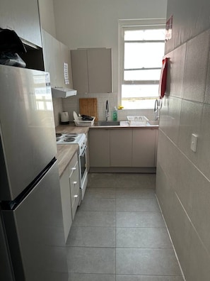 A compact kitchen with a refrigerator, stove, sink, and cabinets. - 5 mins to Central Sydney Lord Raglan Hotel (Alexandria)