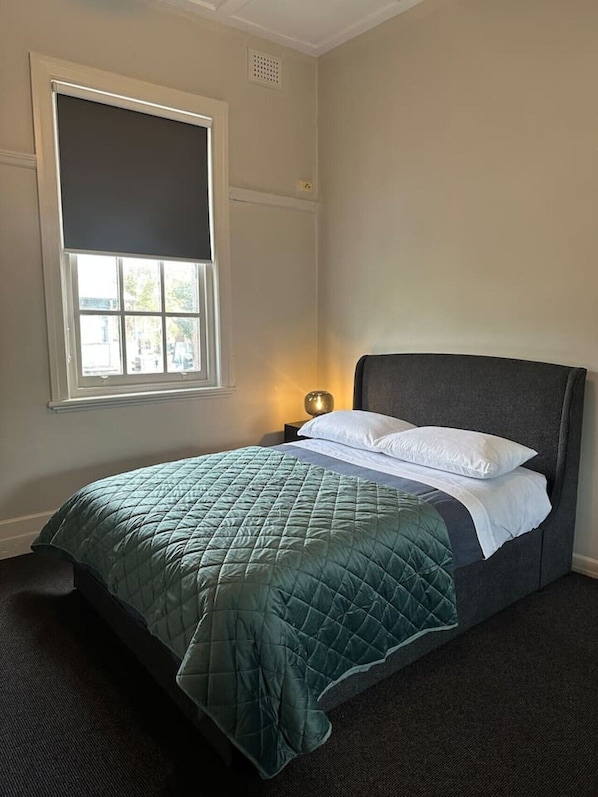 A single bed with a dark headboard, a green quilted bedspread, and two white pillows. There is a window with a white blind partially drawn, and a small bedside table with a lamp. - 5 mins to Central Sydney
Lord Raglan Hotel (Alexandria)