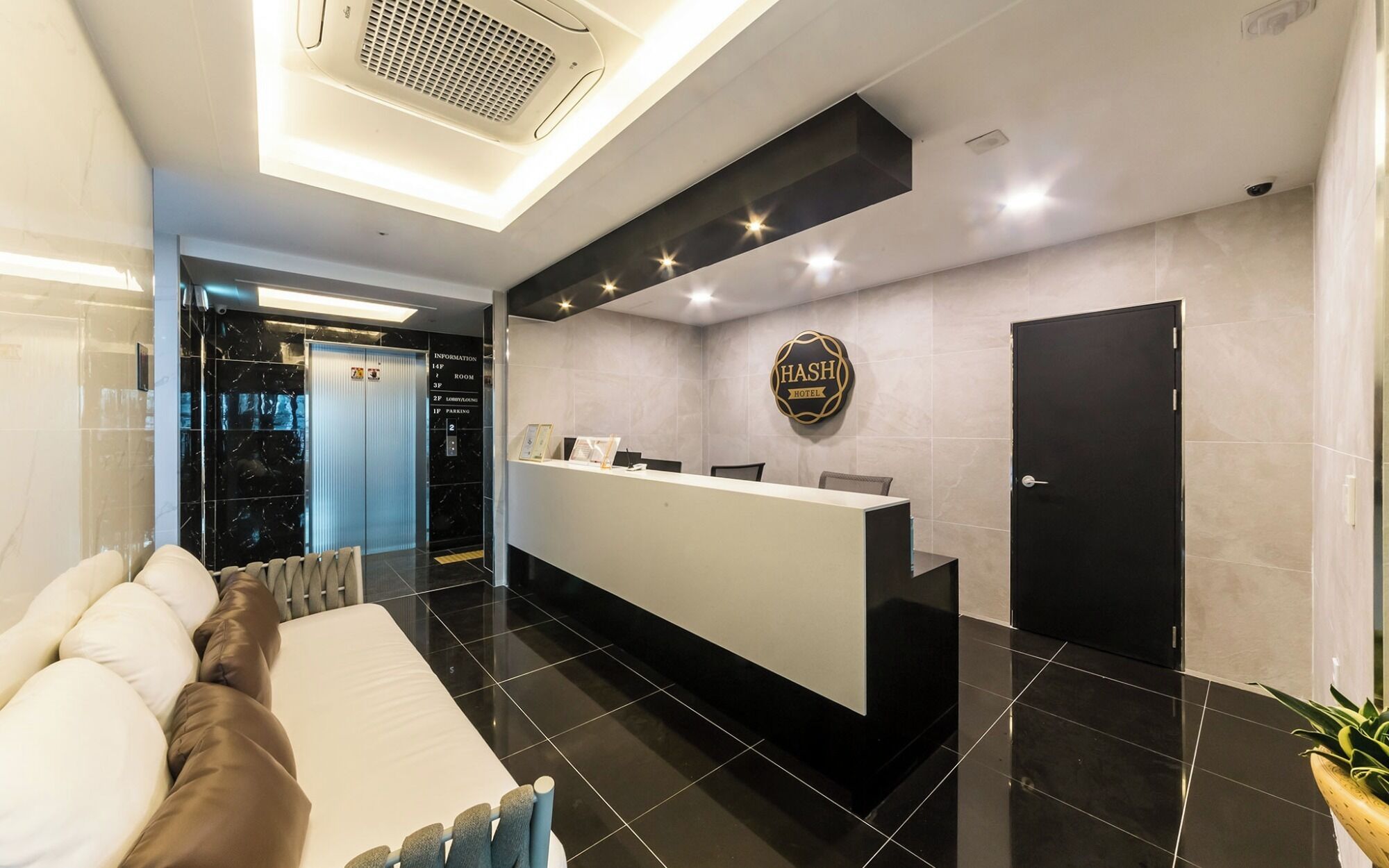 A hotel reception area with a reception desk, a black door, and a sign that reads 'HASH HOTEL'.