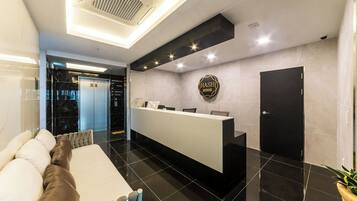 A hotel reception area with a reception desk, a black door, and a sign that reads 'HASH HOTEL'.