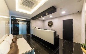 Un'area della reception di un hotel, con una scrivania, una porta nera e un cartello che riporta la scritta 'HASH HOTEL'.