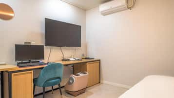 Habitación de hotel con escritorio, dos monitores, una silla, cama, equipo de aire acondicionado y un cesto de basura.