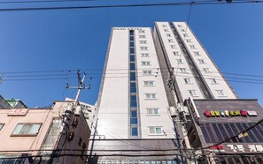 Un palazzo alto con numerosi piani, un cartello ben visibile in cima e diversi pali e fili elettrici.