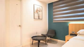 Une chambre d’hôtel comprenant un lit, une table de chevet, une chaise, une œuvre d’art accrochée au mur et une fenêtre avec des stores.